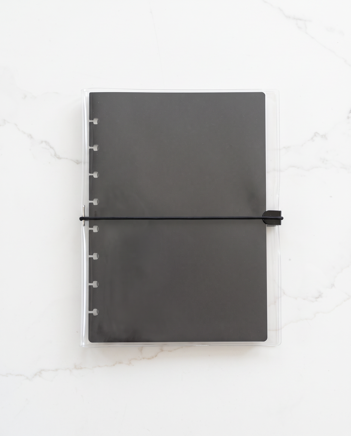 Clear planner binder cover with thin black elastic cord holding a black half letter discbound planner