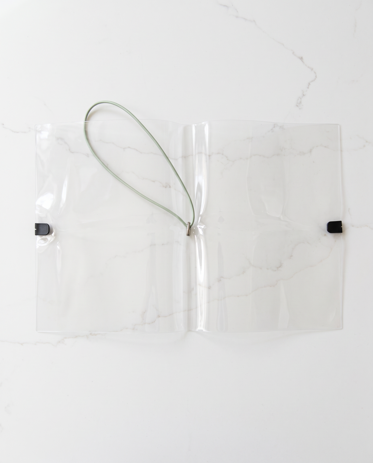 Clear half letter planner binder cover lying open flat with its thin sage elastic cord