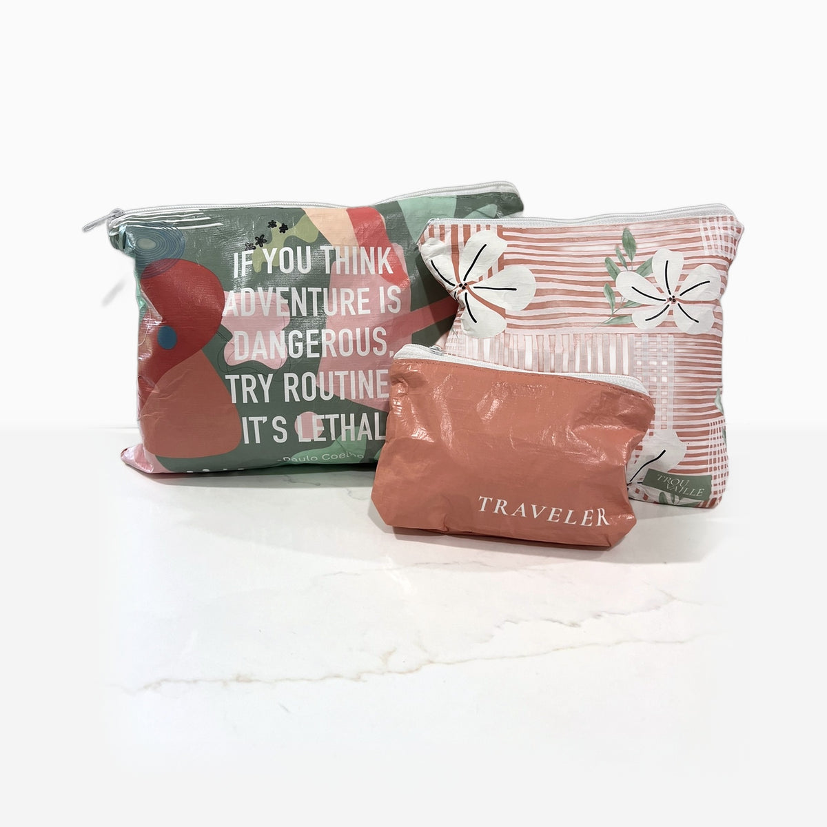 The Coral Trio water-resistant zip pouches on a marble counter: Routine Is Lethal Medium, Coral Flowers Small and Coral Mini