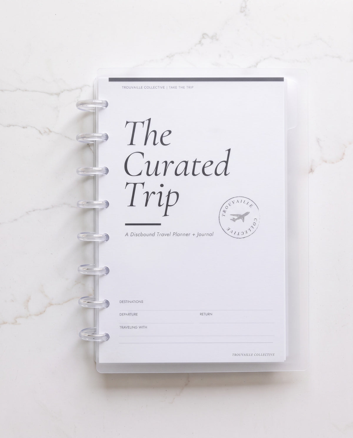 The Curated Trip in the frosted clear discbound binder cover with 8 clear discs on white marble