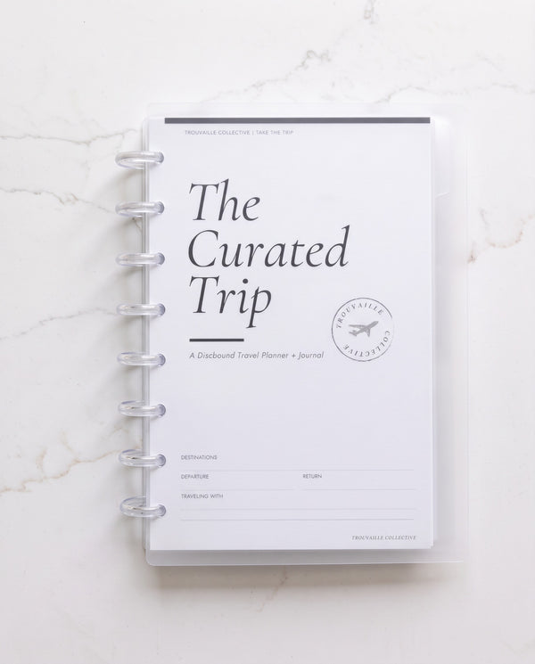 The Curated Trip in the frosted clear discbound binder cover with 8 clear discs on white marble