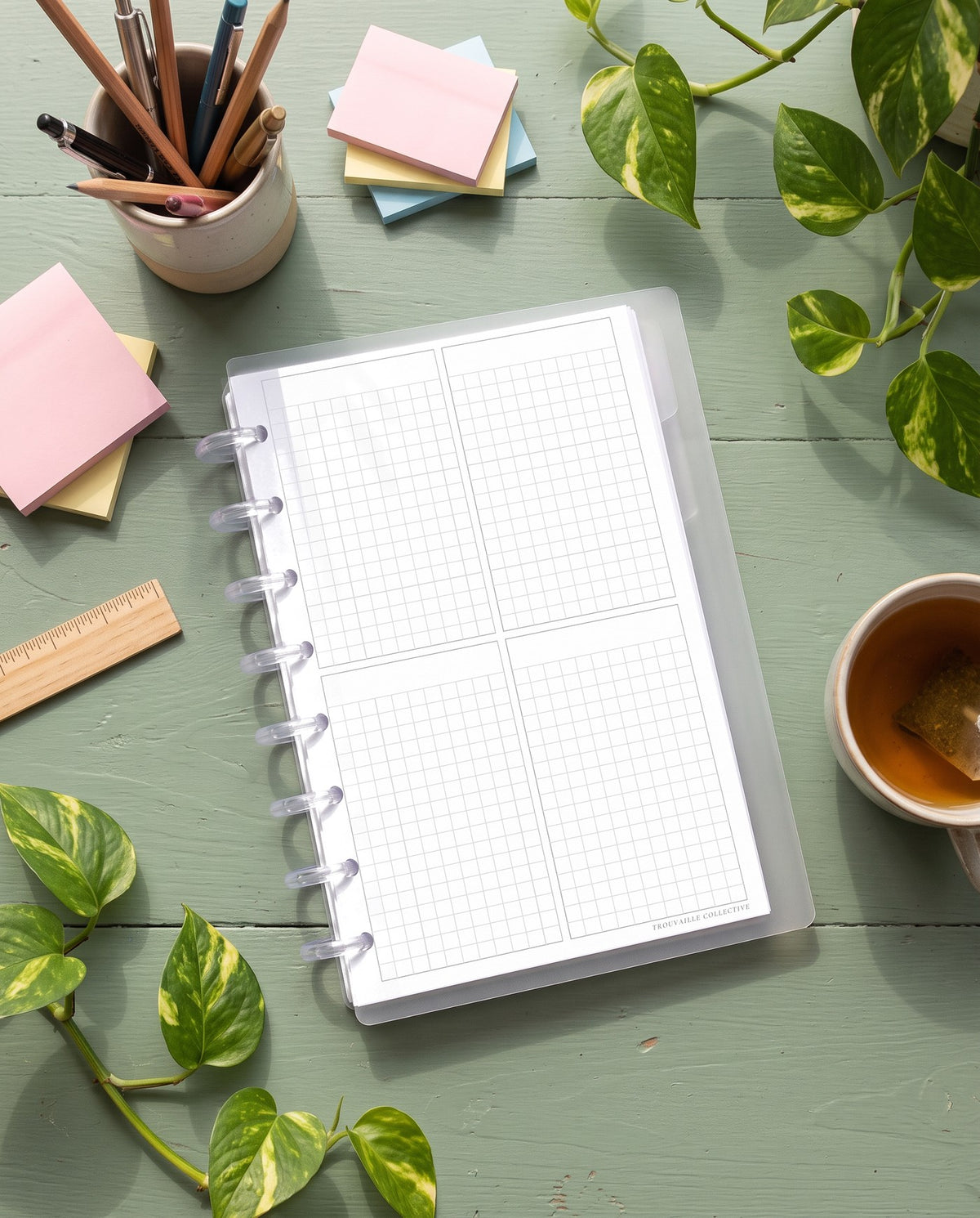Four-Section Grid planner insert inside a clear half letter discbound planner with 8 discs on a sage green desk with pencils and sticky notes