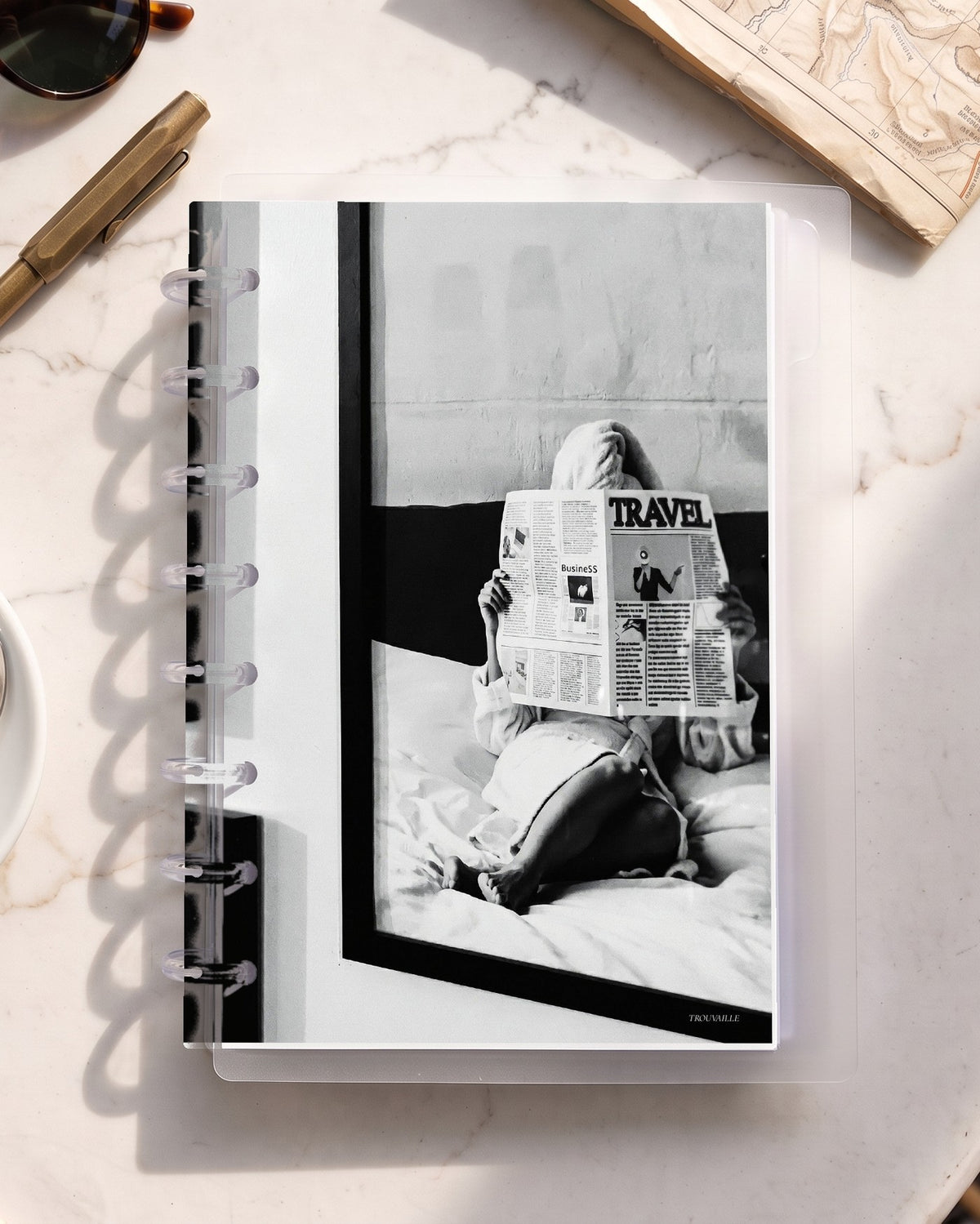 Newspaper cardstock planner dashboard inside a clear half letter discbound planner with 8 discs on a marble cafe table with espresso and a map