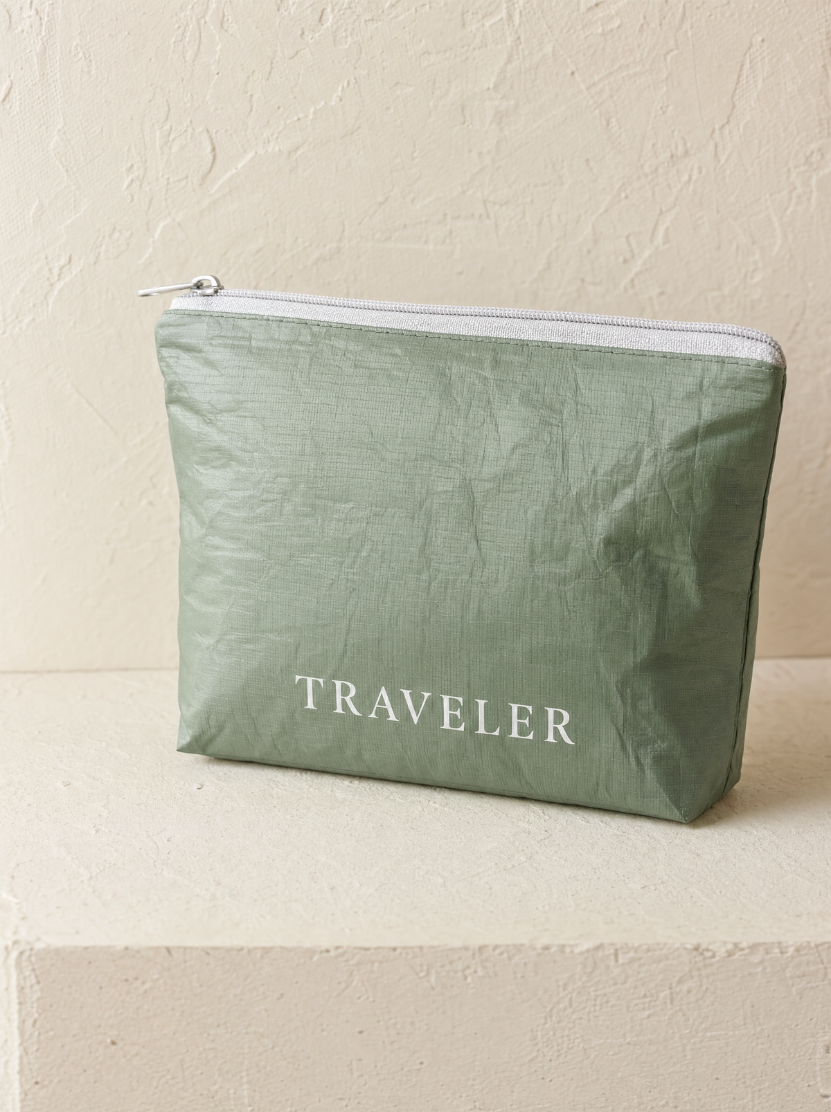 Sage mini water-resistant accessory bag — a solid sage green 6 x 3.75 inch zip travel pouch with TRAVELER printed in white