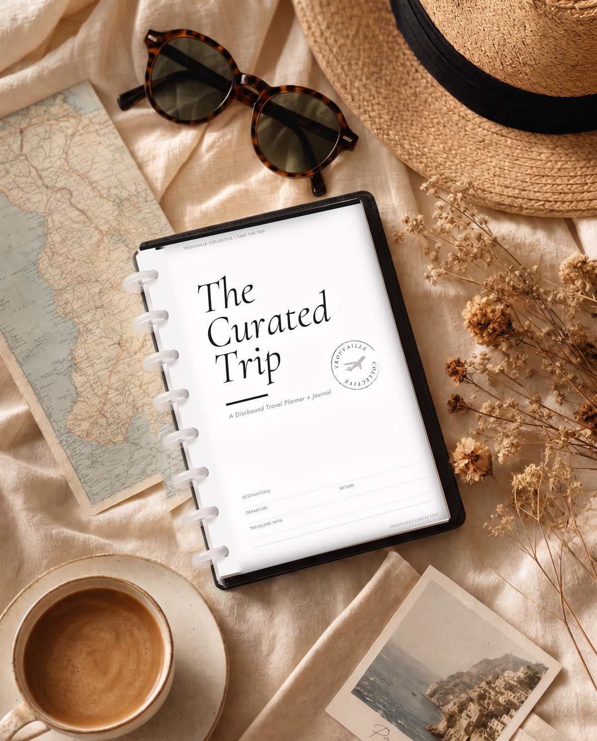 The Curated Trip discbound travel planner and journal with 8 clear discs on a linen flat lay with a map, coffee, sunglasses and a straw hat