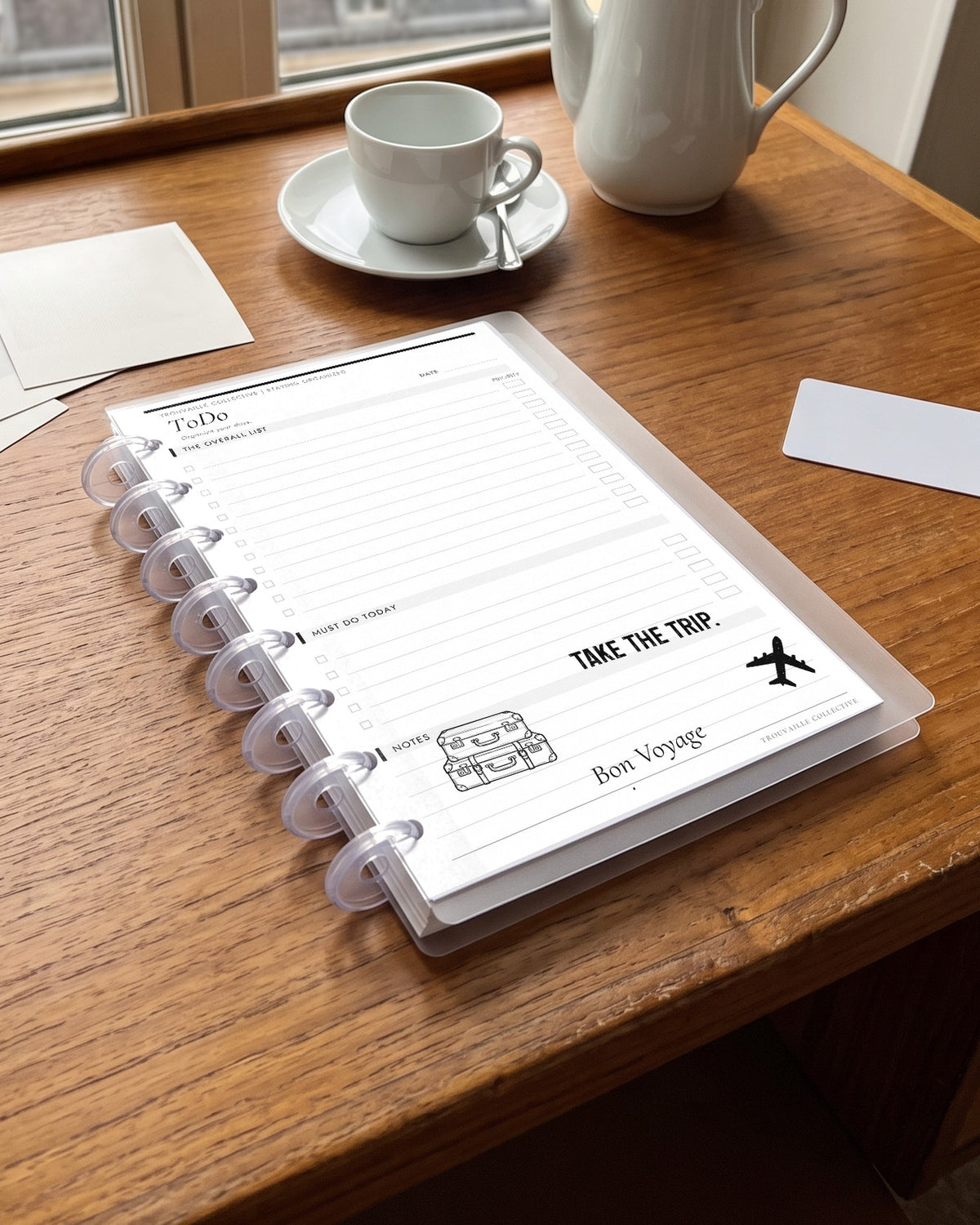 Travel Quotes clear stickers applied to a planner page in a half letter discbound planner on a Paris hotel desk