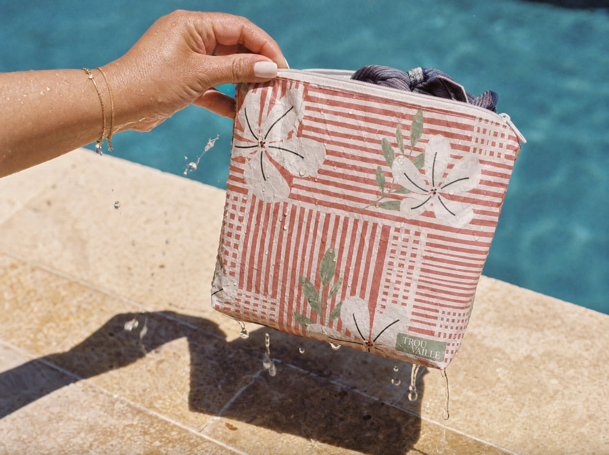 A Trouvaille water-resistant accessory bag held at the edge of a pool with water beading and running off the fabric