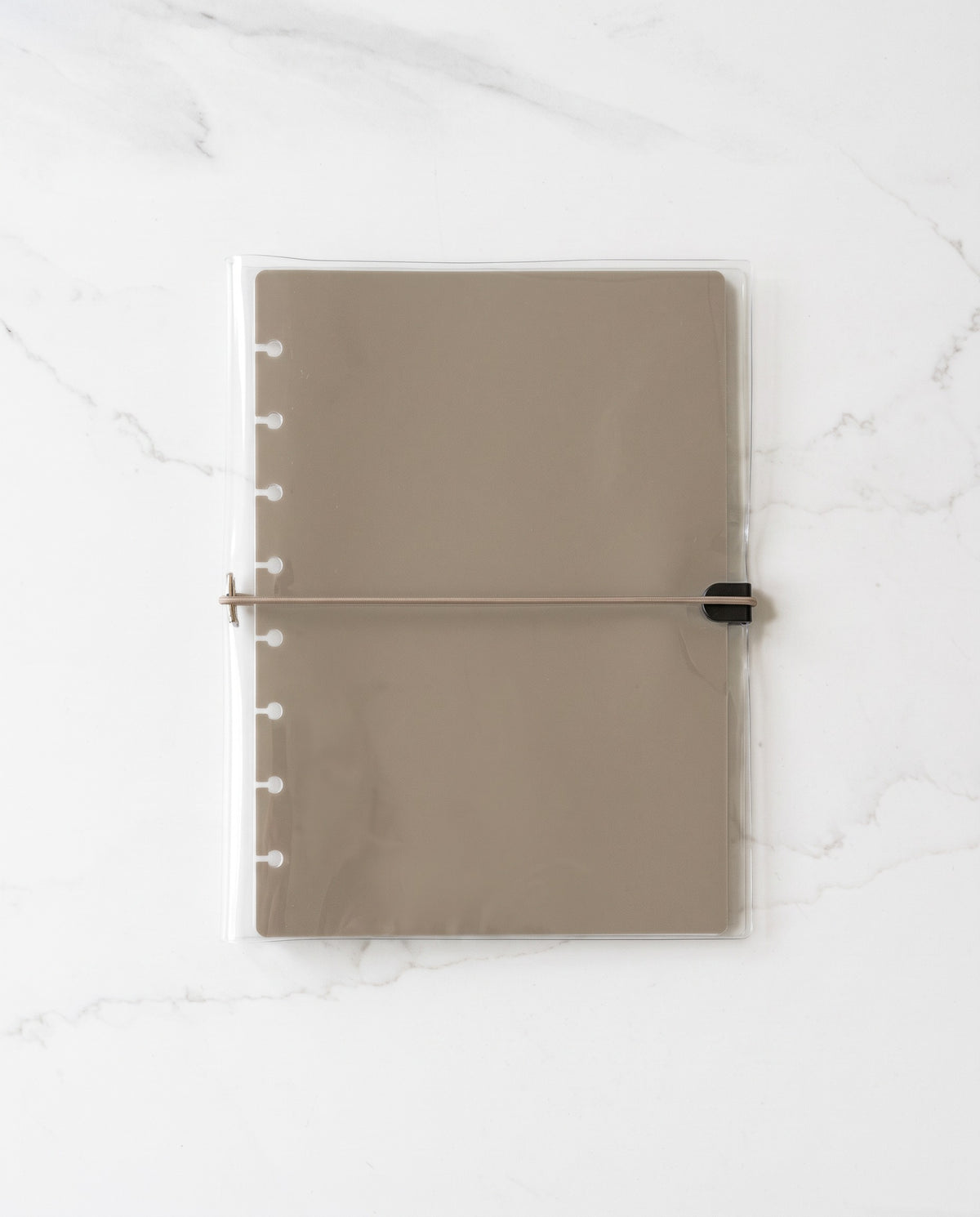 Clear planner binder cover with thin taupe elastic cord holding a taupe half letter discbound planner