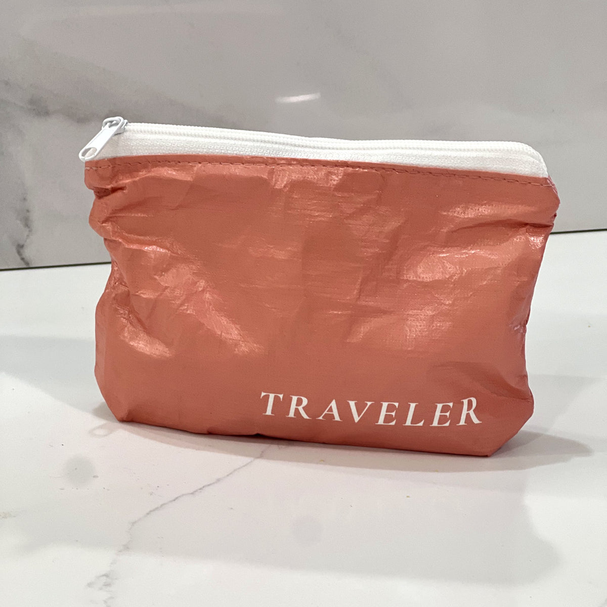 Coral Mini zip pouch sitting on a white marble counter
