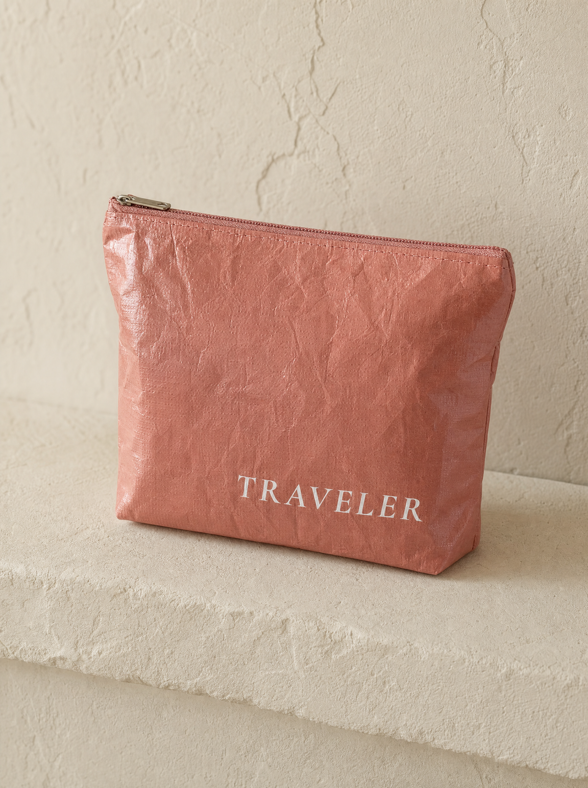 Coral mini water-resistant accessory bag — a solid coral 6 x 3.75 inch zip travel pouch with TRAVELER printed in white