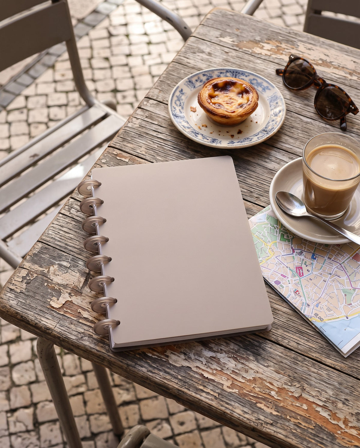 Taupe notebook cover set on a half letter discbound planner with 8 translucent taupe discs, on a Lisbon cafe table with coffee and a pastel de nata