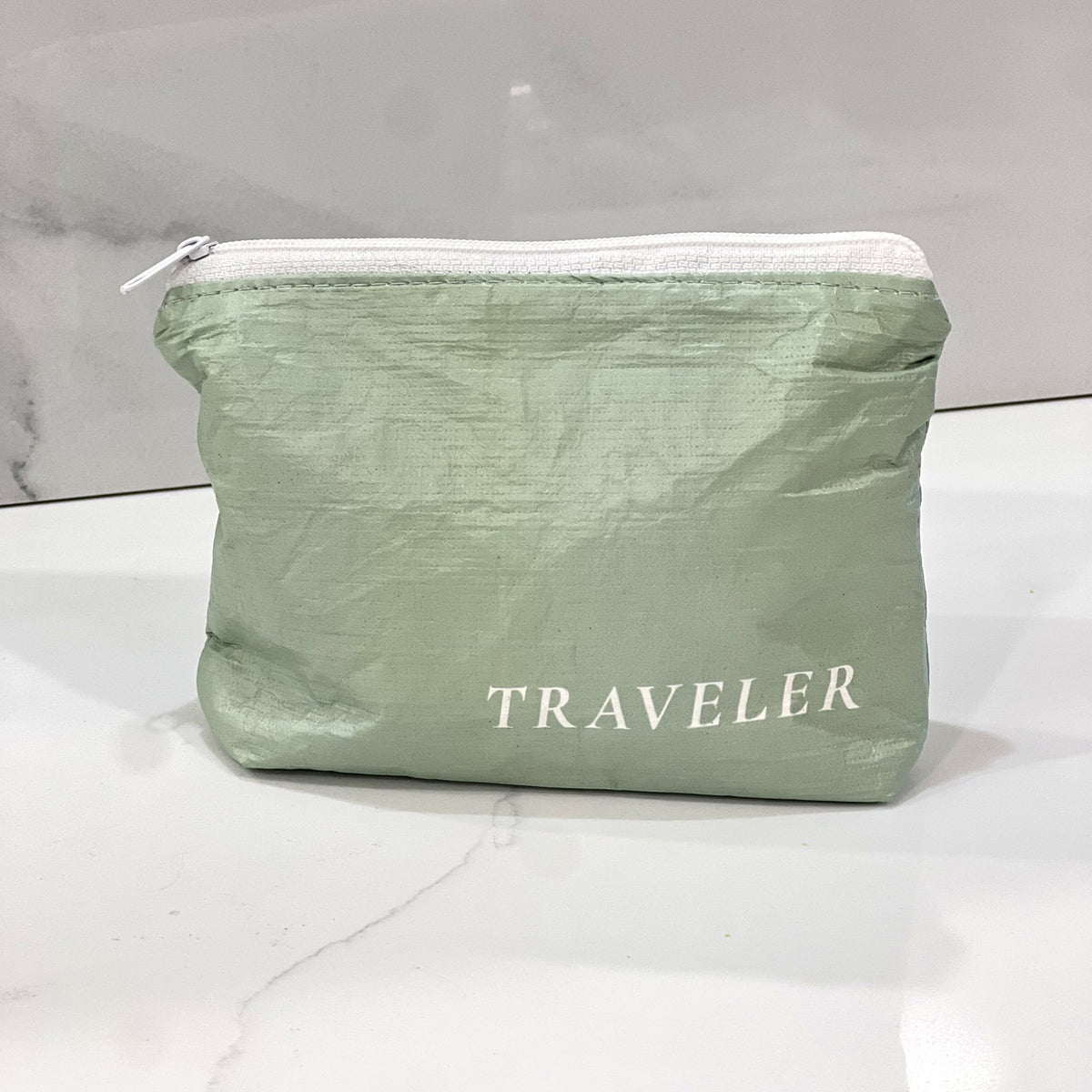 Sage green Mini zip pouch sitting on a white marble counter