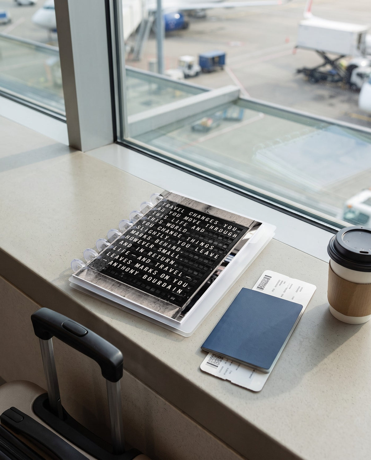 Split-Flap Board cardstock planner dashboard inside a clear half letter discbound planner with 8 discs on an airport gate window ledge with a passport