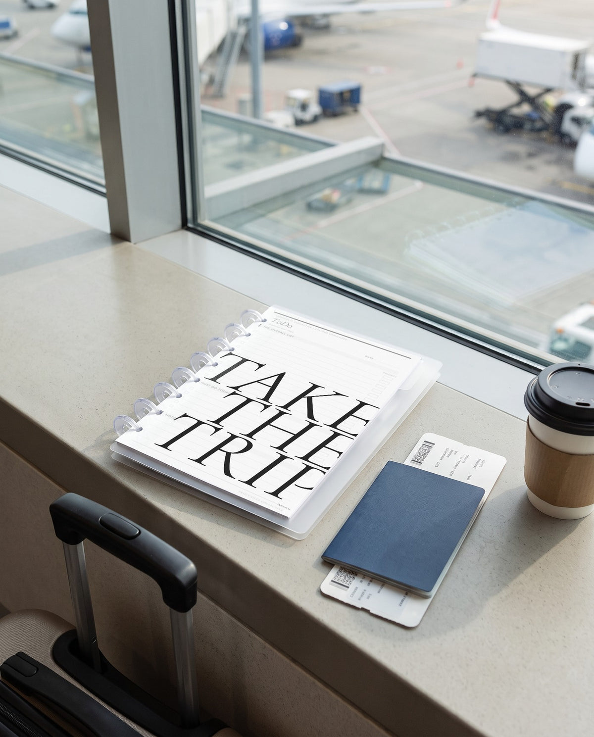 Take the Trip frosted planner dashboard inside a clear half letter discbound planner with 8 discs on an airport gate window ledge with a passport