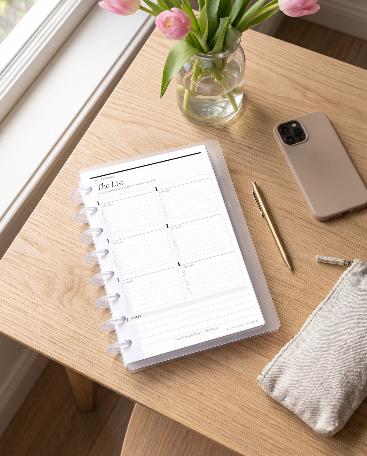 The List planner insert inside a clear half letter discbound planner with 8 discs on an oak desk by a window with tulips