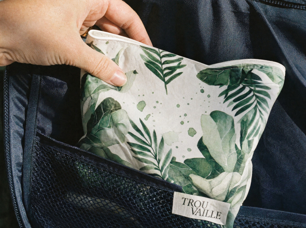 A Trouvaille water-resistant accessory bag being slipped into the mesh pocket of a packed carry-on suitcase