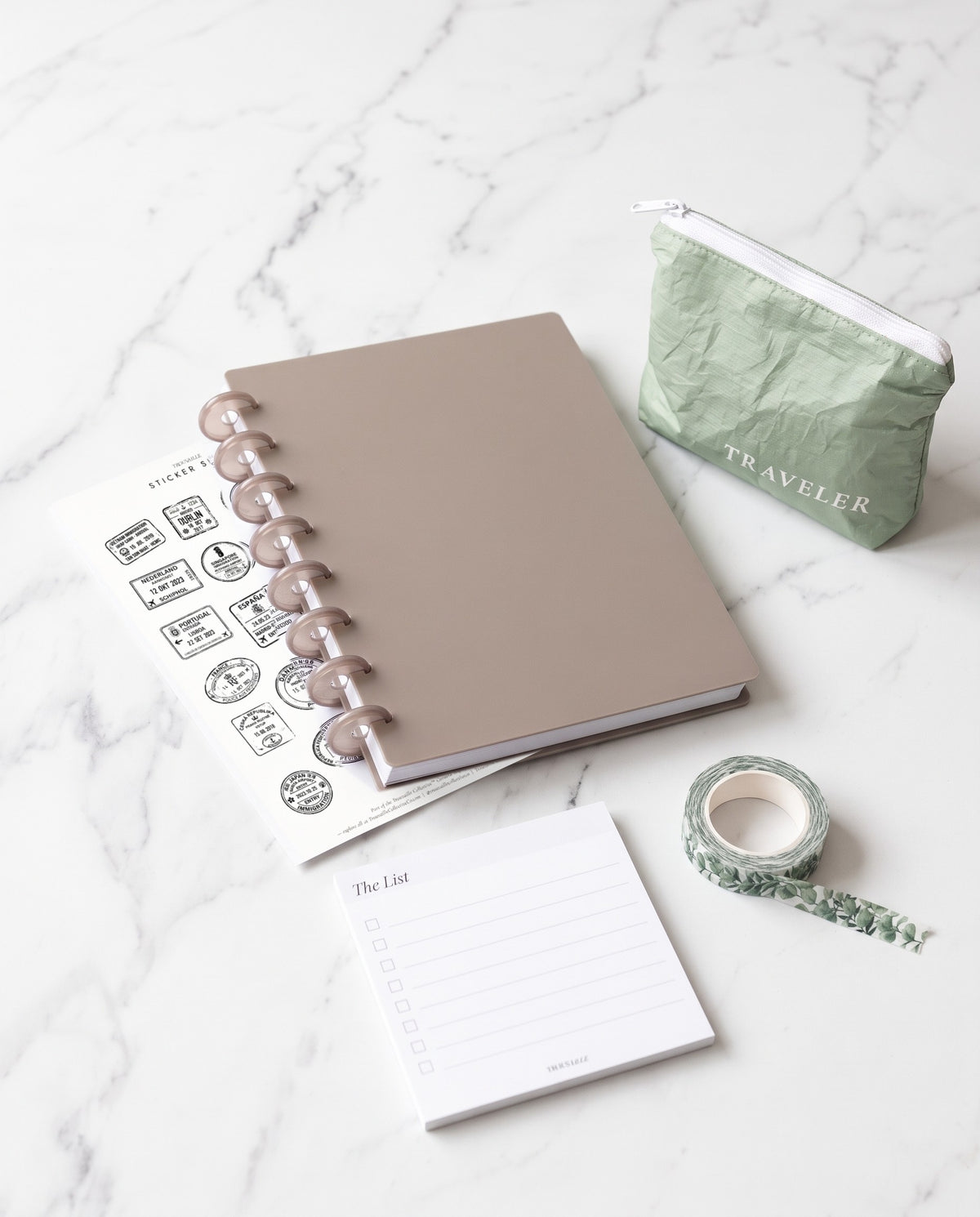 The Whole Planner Gift Set: a taupe half letter discbound notebook with 8 translucent taupe discs, a sage Mini water-resistant pouch, Passport Stamps sticker sheet, The List sticky notes and greenery washi tape on white marble